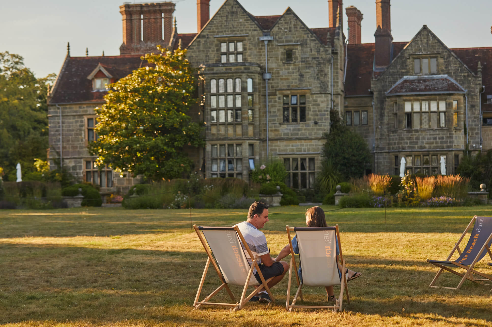 A couple sat in deckchairs in front of the Elizabethan House at Borde Hill.