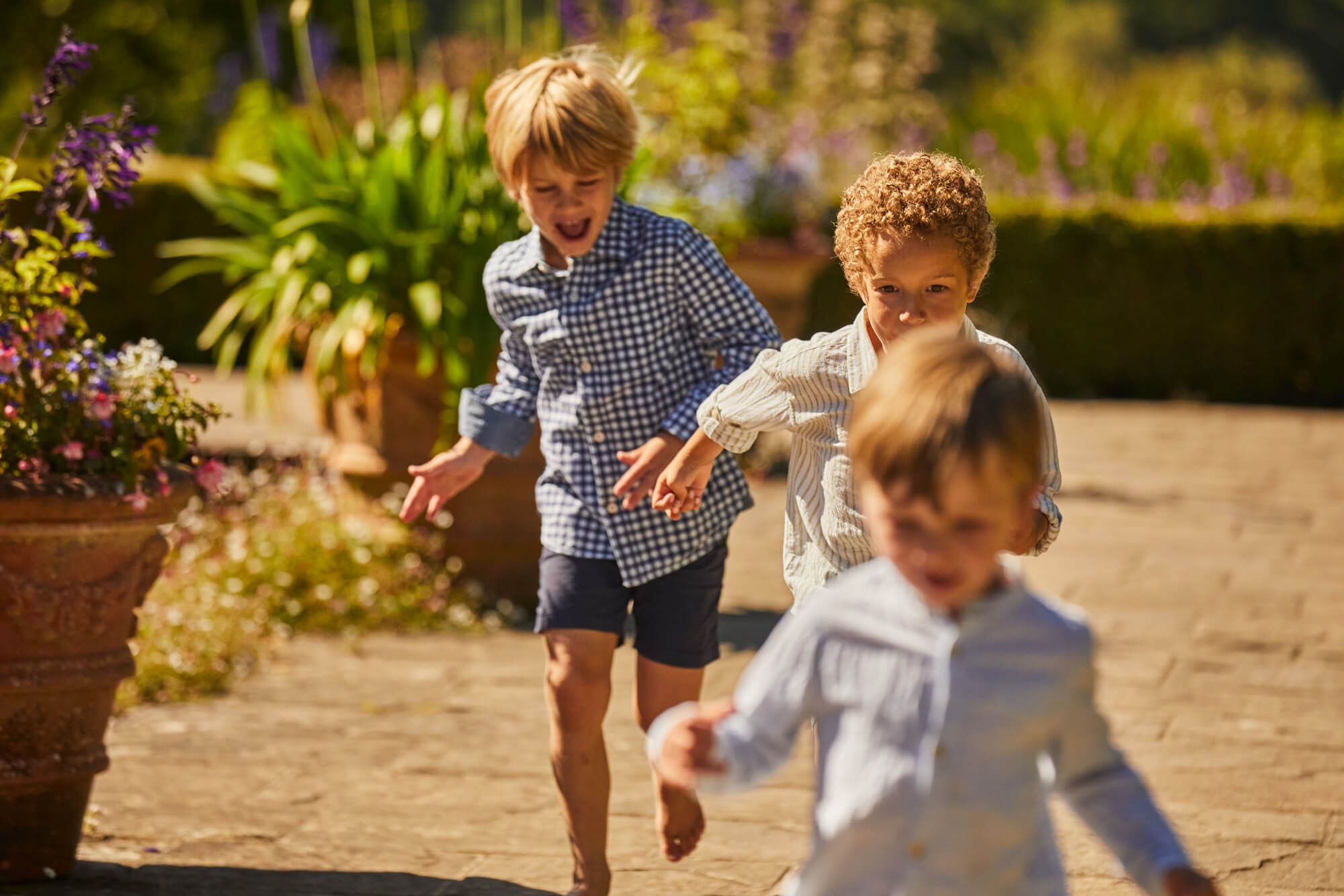 Three children running in the Italian Garden at Borde Hill in summer.